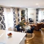 Modern living room with patterned curtains, brown leather chairs, glass dining table, and white countertops overlooking the space.