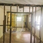 A home interior under renovation, with exposed wooden studs and partial walls, revealing electrical wiring and unfinished spaces.