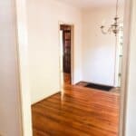 Empty room with hardwood flooring, beige walls, a hanging chandelier, and doorways leading to other rooms in the house.
