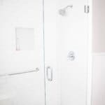 Modern glass shower with white subway tile walls, built-in shelf, and chrome fixtures, including a handle, towel bar, and showerhead.