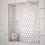 A bottle of bath salts on white hexagonal tile shelf surrounded by rectangular white subway tiles.