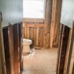 Partially renovated bathroom with exposed wall insulation, a white toilet, and a window with closed blinds.