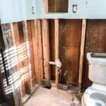 Partially renovated bathroom with exposed wall studs, insulation removed, visible piping, and a toilet positioned to the right.
