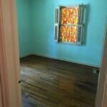 Empty room with light blue walls, hardwood floor, and a window with colorful stained glass and white shutters.
