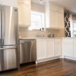 Modern kitchen with stainless steel appliances, white cabinets, light gray backsplash, and dark wood flooring.