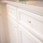 Close-up of white kitchen cabinets with elegant glass knobs and a polished marble countertop.