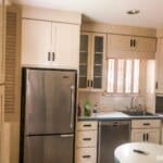 Bright kitchen with stainless steel fridge, dishwasher, cream cabinets, small sink, and a tiled floor. Counter with items on it.