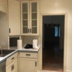Kitchen with beige cabinets, glass-front upper cabinets, a stainless steel sink, and paper towels on the counter. Doorway leads to dining room.