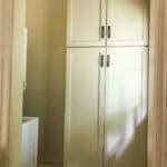 Small utility room with stacked white cabinets and a partially visible washing machine on the left side.