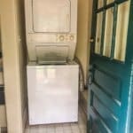 A stacked washer and dryer set in a small laundry room with a tiled floor, next to an open green door.