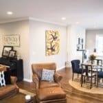 Modern living area with brown leather chairs, a piano, colorful artwork, and an adjoining kitchen with a glass dining table.
