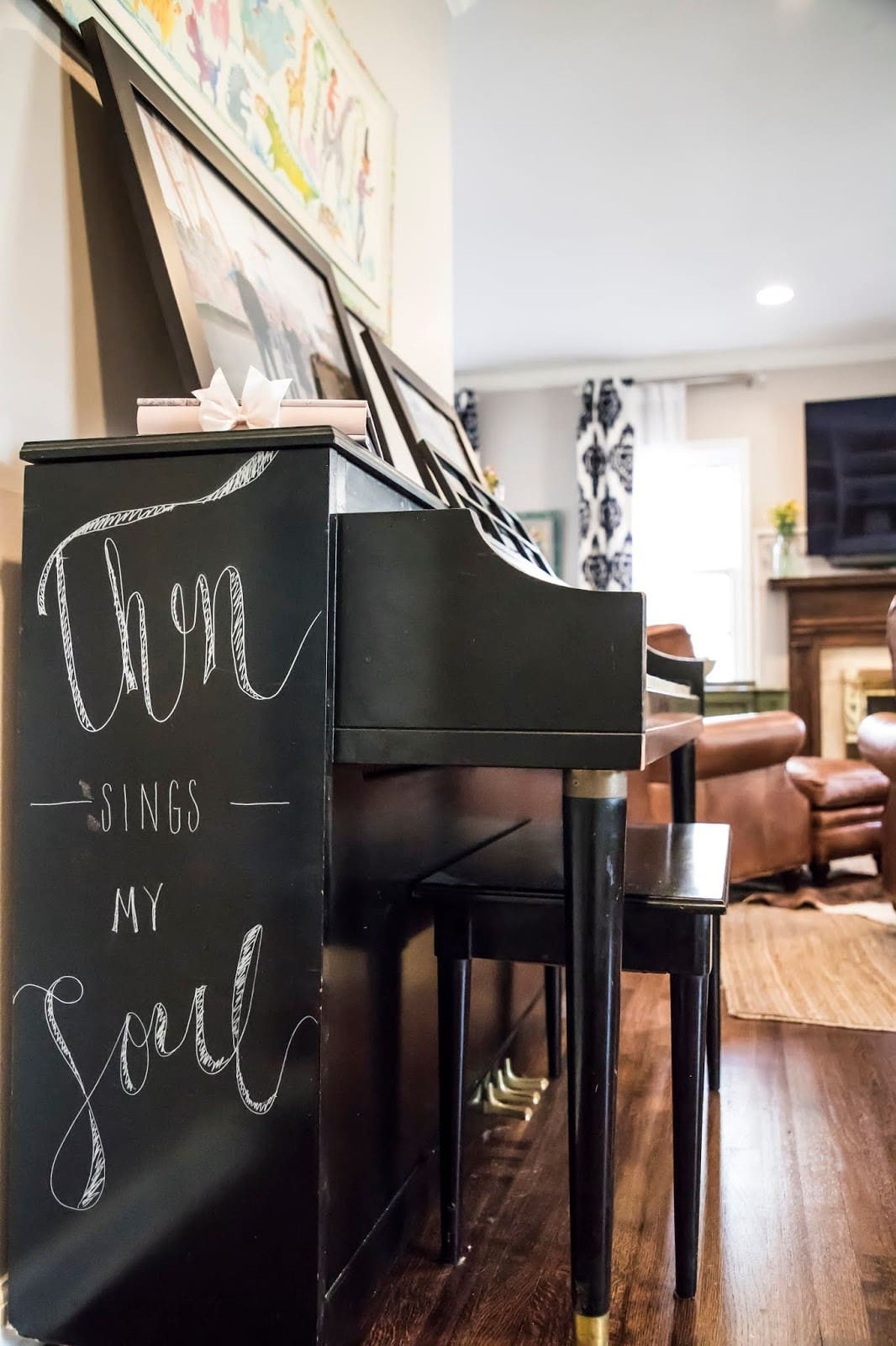 Black piano with words "Then sings my soul" written on its side, in a cozy living room with brown leather chairs.