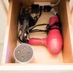Open drawer with a hairdryer, curling iron, smart speaker, and a power strip inside.