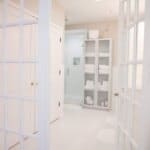 A bright, elegant bathroom with glass doors, modern shower, white storage cabinet with towels, and a white tiled floor.