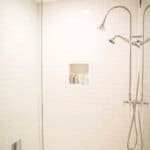 Spacious modern shower with white subway tiles, dual showerheads, a built-in tiled niche with toiletries, and a frameless glass door.