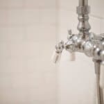 Close-up of a vintage-style silver shower faucet with white tiles in the background.