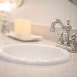 Close-up of a modern bathroom sink with a chrome faucet, white candle on a tray, and a decorative cup on the countertop.