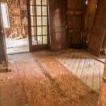 Partially renovated room with exposed wooden studs and insulation, a window on the far side, and French doors leading to another area.