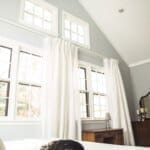 Cozy bedroom with white curtains and vaulted ceiling, featuring a cat sleeping on a neatly made bed.