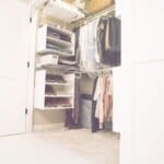 Organized walk-in closet with hanging clothes, shelves for shoes, baskets, and storage bins on beige carpet.